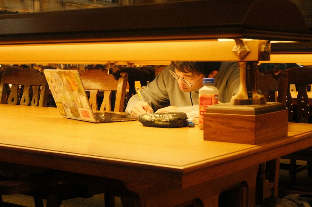 Student working with a laptop and notebook in a library